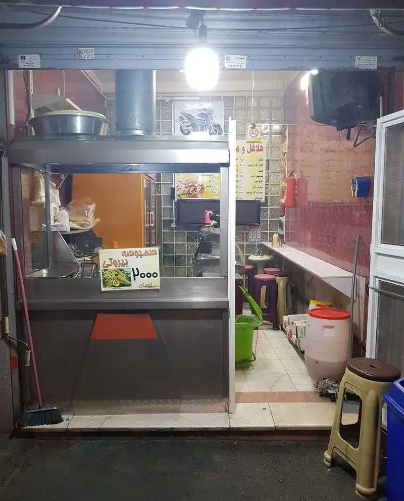 فضای داخلی پیتزا دلخواسته، ارائه دهنده فلافل و سمبوسه بیروتی، با کانتر پذیرایی و منوی آشکار غذاها برای مشتریان.