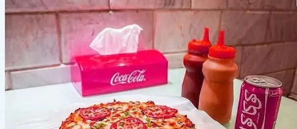 پیتزا خوشمزه رستوران متئو با برش‌های گوجه و فلفل، در کنار نوشابه کوکاکولا صورتی، سس کچاپ و جعبه دستمال.
