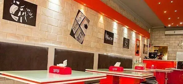 نمایی از دکوراسیون داخلی مدرن رستوران متئو با دیوار آجری، رنگ‌های شاد نارنجی، میز و صندلی‌های راحت و فضای غذاخوری دلنشین.