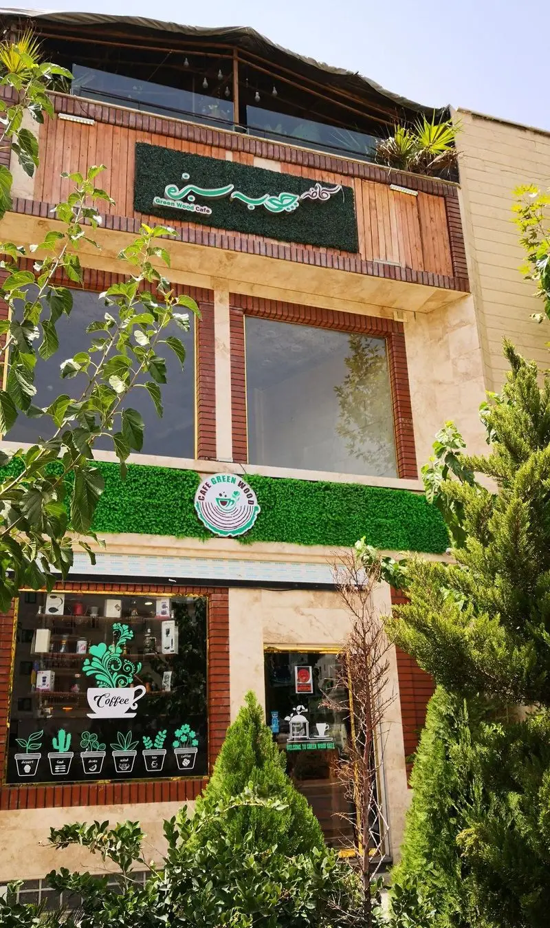 نمای جلوی کافه چوب سبز (Green Wood Cafe) با طراحی چشم‌نواز شامل تابلوهای سبز، لوگو و تزئینات گیاهی مدرن.