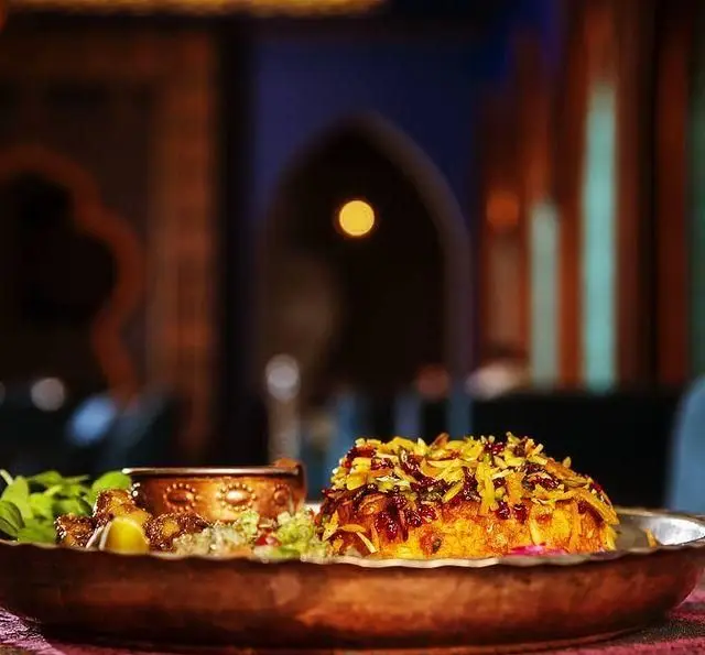 کافه رستوران آهون: غذای سنتی و لذیذ ایرانی، ته چین زرشک و پسته، سرو شده در بشقاب مسی، در فضایی گرم و دلنشین.