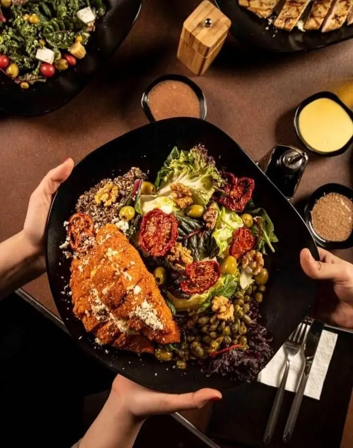 سفره رنگارنگ بالکافه با غذای اصلی شنیتسل مرغ یا ماهی ترد، سالاد تازه، کینوا، زیتون، گردو و گوجه خشک. یک تجربه غذایی سالم و لذیذ.