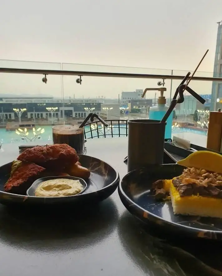 تجربه لذت‌بخش غذای ایرانی و بین‌المللی در بالکافه با منظره‌ای دلنشین. مرغ سوخاری، چلوگوشت و نوشیدنی در فضای باز کافه.