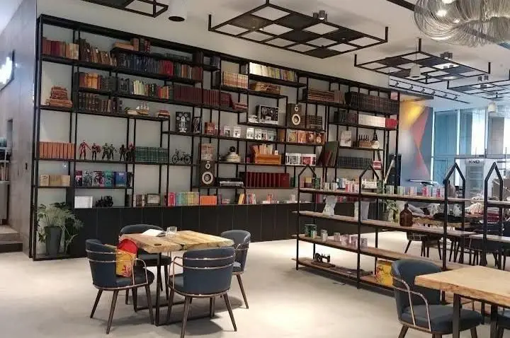 فضای دنج و مدرن بالکافه با قفسه‌های بلند کتاب و میزهای چوبی. ایده‌آل برای مطالعه، کار یا صرف قهوه در محیطی آرام.