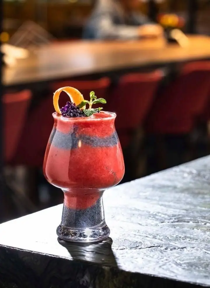 نوشیدنی لایه ای قرمز و تیره بالکافه با طعم میوه ای، تزئین شده با توت سیاه، نعناع تازه و پوست پرتقال، انتخابی دلپذیر.