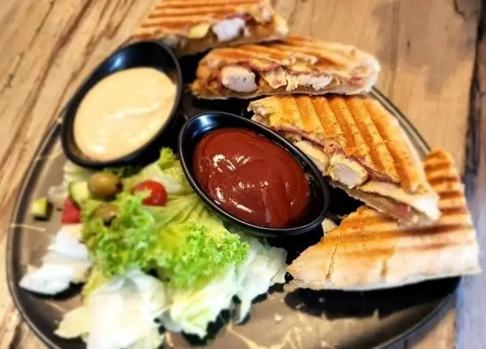 پانینی مرغ و پنیر گریل شده بالکافه با سالاد سبزیجات تازه، زیتون و گوجه فرنگی، همراه با سس کچاپ و سس مخصوص، انتخابی دلپذیر در منوی کافه.