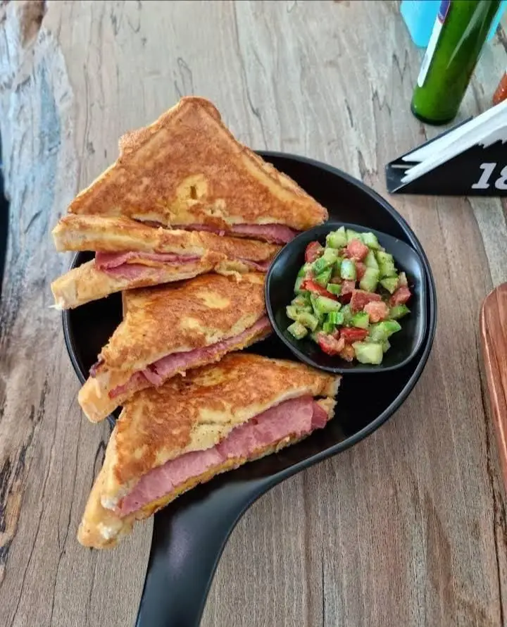 ساندویچ‌های فرنچ تست طلایی بالکافه با ژامبون و سالاد تازه خیار و گوجه. غذایی لذیذ روی میز چوبی کافه.