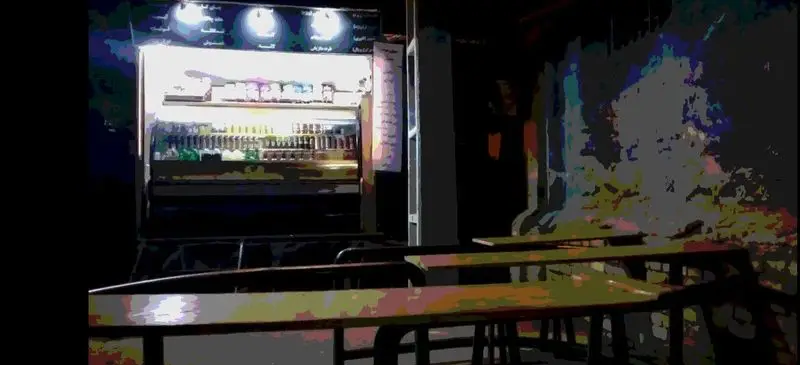 تصویری از فضای داخلی کافه فست فود سورنا سیار، نمایشگر روشن نوشیدنی‌ها و منو، همراه با میز و صندلی‌های چوبی برای مشتریان.