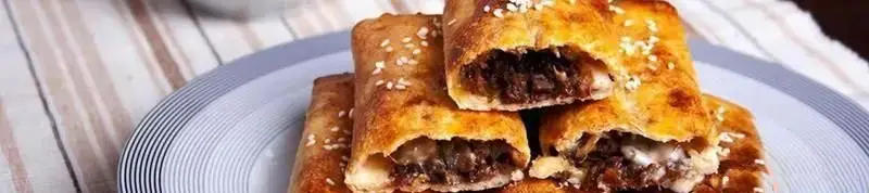 تصویری از رول‌های بورک طلایی و برشته، پر شده با مغز دلچسب گوشت و پنیر، تزئین شده با کنجد در رستوران بورک. یک غذای لذیذ و محبوب.