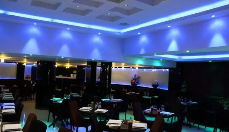 فضای داخلی مدرن و شیک رستوران آروما با نورپردازی آبی و سبز، میزهای چیدمان شده و صندلی‌های راحت، فضایی دلنشین برای صرف غذا.