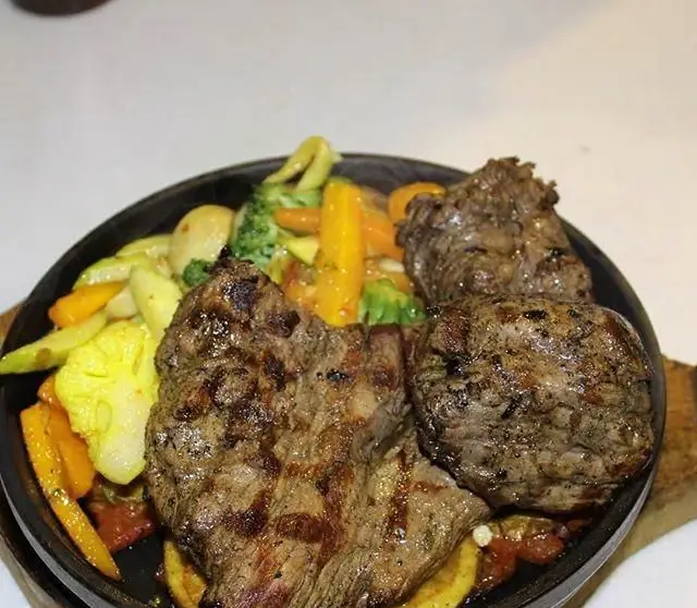 استیک گریل شده آبدار و لذیذ همراه با سبزیجات تازه شامل هویج، کلم بروکلی و کلم گل، در سینی داغ رستوران آروما.