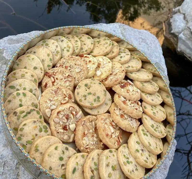 سینی بزرگ و زیبای شیرینی‌های میکس تازه کافه گرین (موزه مقدم)، شامل کوکی‌های پسته و بادام خوش‌طعم برای پذیرایی.