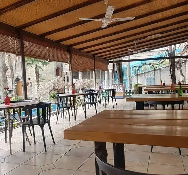 نمایی از فضای دلنشین و سرسبز کافه گرین در محوطه موزه مقدم؛ کافه‌ای با سقف چوبی، میز و صندلی‌های مدرن برای لحظاتی آرام.