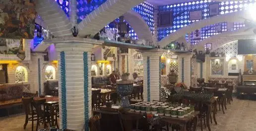 فضای داخلی کافه قلیان پیر بابا با دکوراسیون سنتی و نورپردازی آبی، محیطی دلنشین برای مشتریان در حال گفتگو و استراحت.