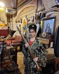 دختری با لباس محلی و تفنگ قدیمی در دکوراسیون اصیل کافه قلیان پیر بابا؛ تجربه ای دلنشین در کافه سنتی.