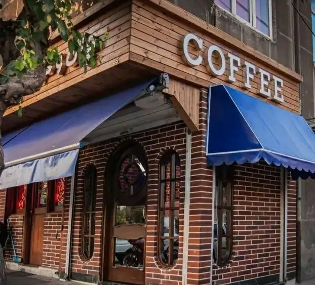 نمای زیبای بیرونی کافه چای و قهوه حاج رضا با دیوارهای آجری قهوه‌ای، سایبان‌های آبی و تابلوی COFFEE چوبی.