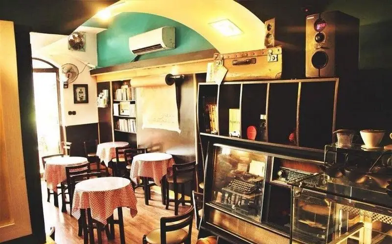 فضای داخلی کافه گرامافون با دکوراسیون وینتیج منحصر به فرد، شامل کتابخانه غنی، میزهای شطرنجی و پیشخوان مجهز.