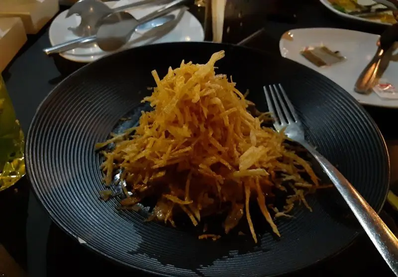 نمای نزدیک از دیشی خوشمزه در کافه روژه شامل خلال سیب‌زمینی برشته و طلایی سرو شده روی بشقاب تیره با چنگال آماده برای خوردن.