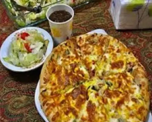 میز غذای کامل از فست فود پیتزا و ساندویچ گلها شامل پیتزای گرم و پنیردار، سالاد کاهو و گوجه فرنگی، و نوشیدنی دلچسب.