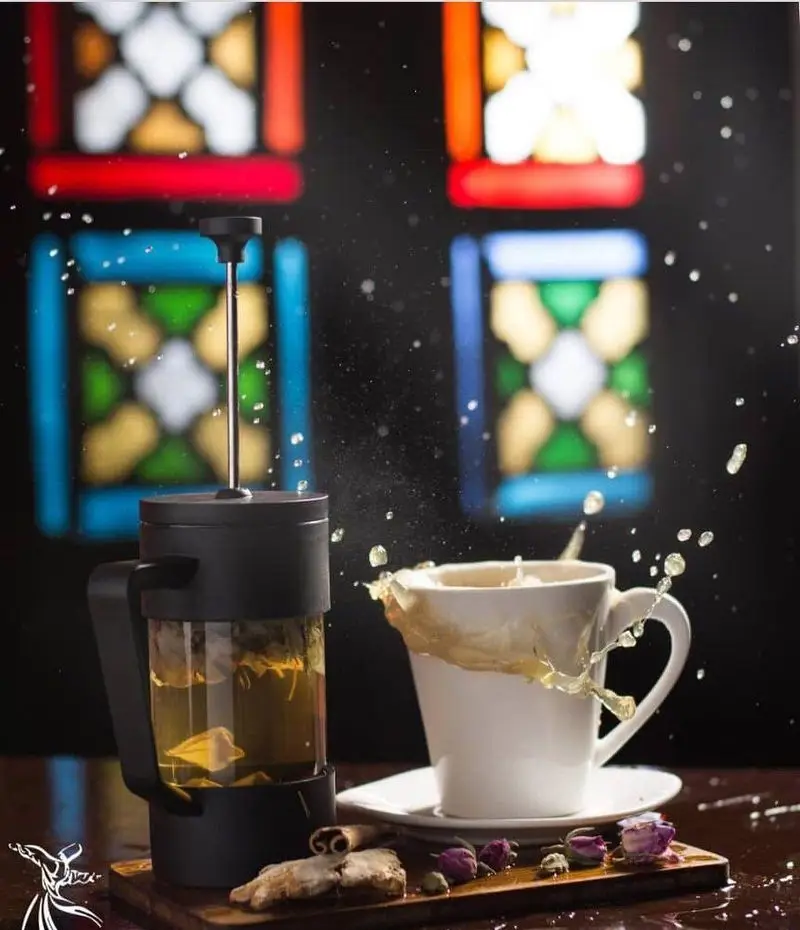 دمنوش و چای داغ در فرنچ پرس شیک کافه رستوران درویش، با ماگ چای در حال پاشش و ادویه‌های معطر زنجبیل، دارچین و گل محمدی.