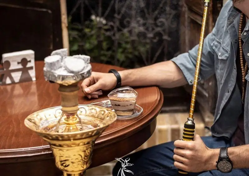 تصویری از مشتری در کافه رستوران درویش که از قلیان و دسری خوشمزه لذت می برد. تجربه ای دلپذیر در فضایی آرامش بخش.