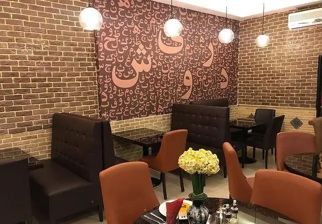 کافه رستوران درویش: فضای داخلی با دیوارهای آجری، دیوارپوش حروف فارسی و عربی، میز و صندلی‌های شیک، محیطی دنج و آرام.