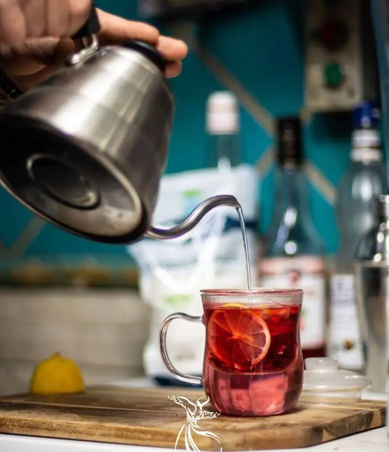 آماده‌سازی دمنوش گرم و تازه در کافه رستوران درویش: ریختن آب جوش از کتری مدرن به لیوان حاوی لیمو برای نوشیدنی دلچسب و آرامش‌بخش.