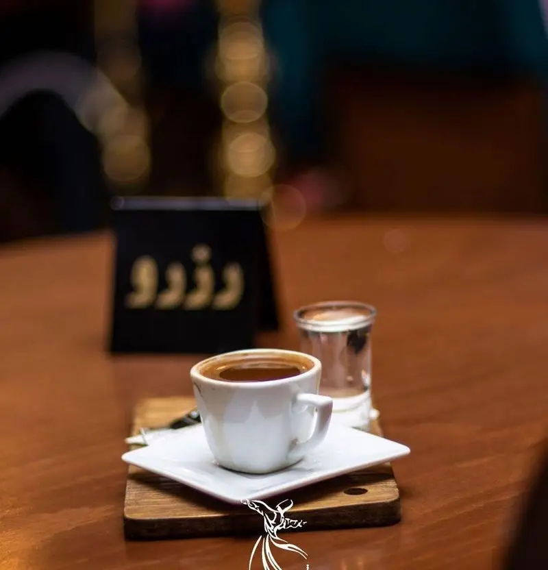 تصویری از یک فنجان قهوه ترک داغ و معطر در کافه رستوران درویش، سرو شده با لیوان آب روی میز چوبی در فضایی دلنشین و دنج.