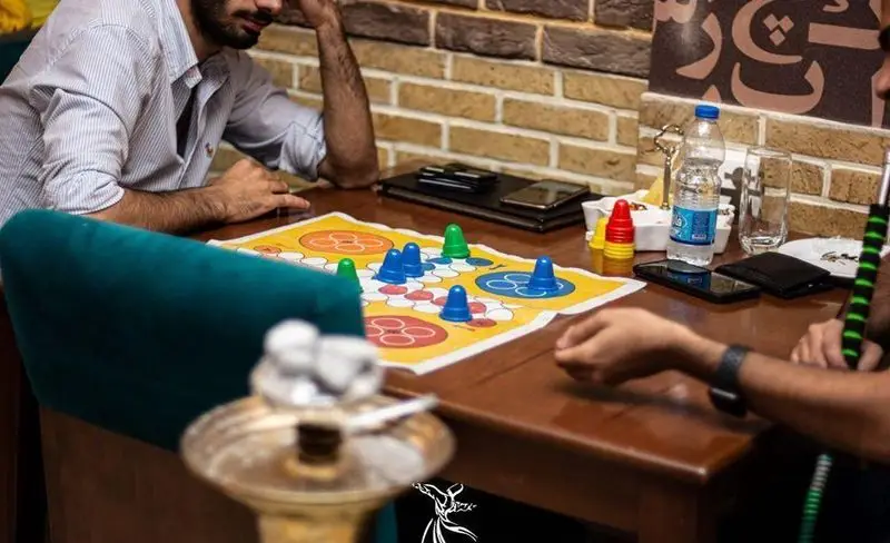 تصویری از مشتریان کافه رستوران درویش در حال بازی منچ و قلیان، فضایی دلنشین برای دورهمی دوستانه و استراحت.