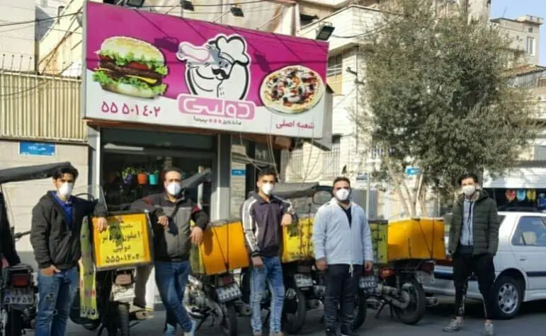 تصویری از کارکنان ساندویچی دولپی (شعبه اصلی) با ماسک و موتورهای پیک موتوری آماده تحویل غذا؛ شامل بهترین همبرگر و پیتزا.
