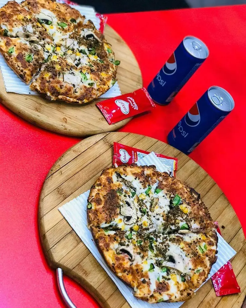 دو پیتزای خوشمزه از ساندویچی دولپی با ترکیبات مرغ، قارچ و ذرت روی تخته چوبی، همراه با پپسی و سس کچاپ.