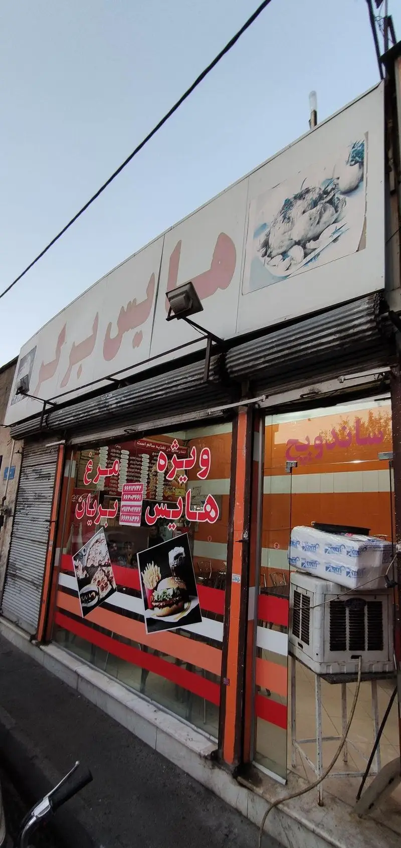 نمای بیرونی فست فود هایس برگر با تابلوی بزرگ و عکس پیتزا و ساندویچ، متخصص مرغ بریان و برگرهای خوشمزه.