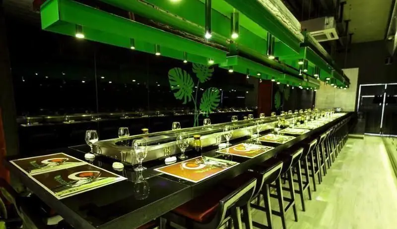 فضای داخلی شیک و مدرن سوشی بار آووکادو با میز بلند سوشی، صندلی‌های بار و دکوراسیون سبز و مشکی. محیطی آرام و جذاب برای تجربه سوشی.