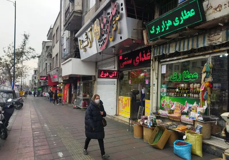 خیابان پر جنب و جوش تهران با آش علی بابا (غذای سنتی) و عطاری هزار برگ. مردم در حال خرید از کسب و کارهای محلی.