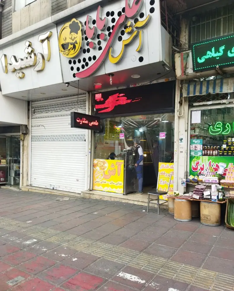 تصویر کسب و کار آش علی بابا در ایران، با تابلوهای نئون و ویترین پر از آش رشته و انواع غذای سنتی و سالم.