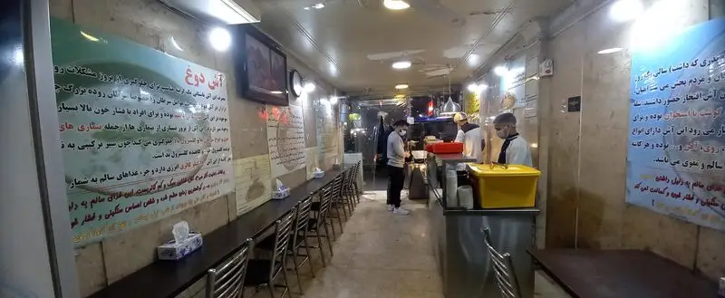 فضای داخلی آش فروشی آش علی بابا، با میز و صندلی‌های منظم و کارکنان در حال آماده‌سازی آش دوغ و سایر غذاهای سنتی ایرانی.
