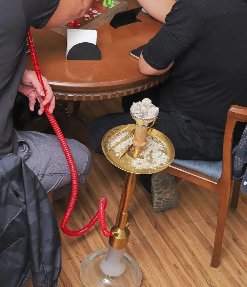 دورهمی دوستانه در کافه بینج با قلیان و بازی رومیزی روی میز چوبی. لذت لحظات شاد و آرامش‌بخش در محیط دنج کافه.