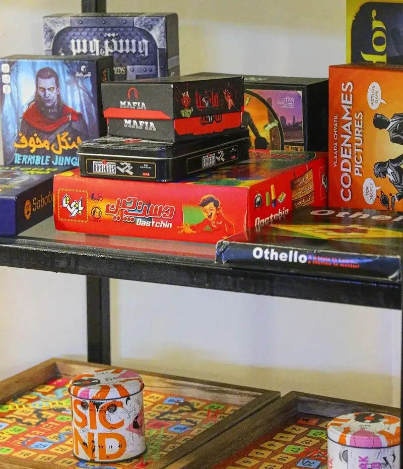 قفسه‌ای جذاب از بازی‌های رومیزی متنوع و پرطرفدار (مانند مافیا، کدیمز و دستچین) در کافه بازی بینج، ایده‌آل برای سرگرمی و دورهمی.