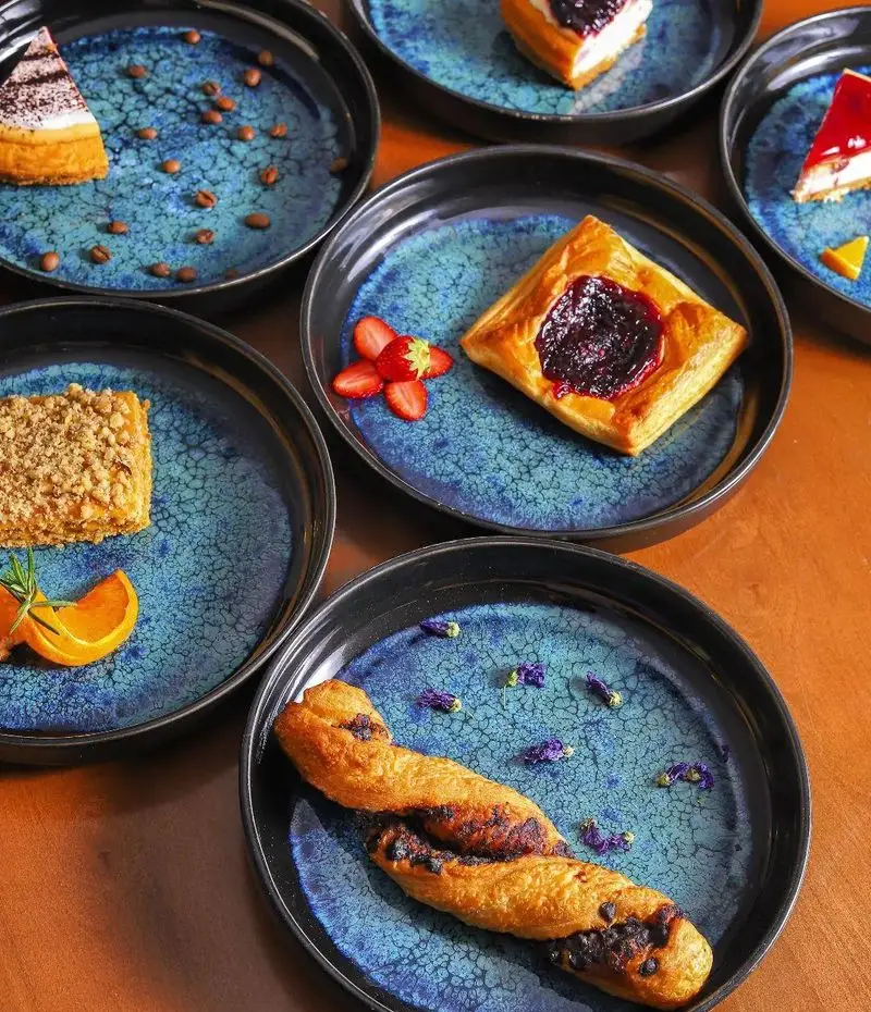 انواع دسرهای لذیذ کافه بینج: کیک، پای میوه، شیرینی و دسر کرمبل با ظروف آبی جذاب، انتخابی ایده‌آل برای عصرانه و صبحانه.