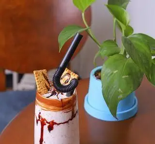 میل شیک خوشمزه و خنک با تزئین کراکر و سس شکلات در کافه بینج. تجربه نوشیدنی‌های جذاب و دسرهای تازه کافه بینج در محیطی آرام.