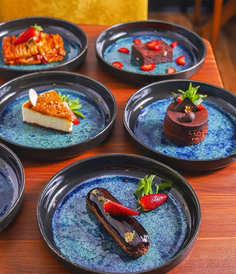 پذیرایی با دسرهای متنوع کافه بینج: چیزکیک با سس کارامل، کیک‌های شکلاتی، اکلر و شیرینی‌های جذاب با توت فرنگی تازه.