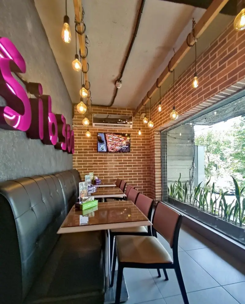 رستوران پیتزا سیب ۳۶۰: فضای داخلی دنج و مدرن با دیوارهای آجری، نورپردازی گرم، نیمکت چرمی و لوگوی برجسته سیب۳۶۰