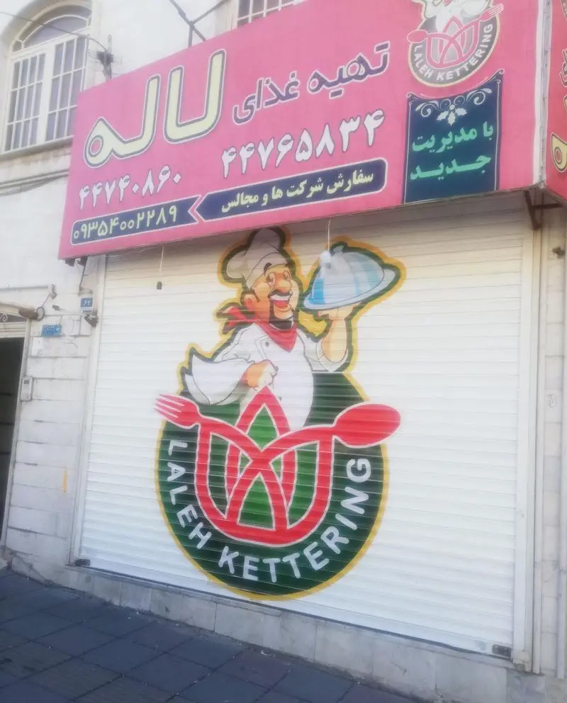 تصویر نمای بیرونی کترینگ لاله با تابلو صورتی رنگ حاوی "تهیه غذای" و شماره تلفن‌ها. لوگوی سرآشپز و عبارت "Laleh Kettering" روی کرکره.