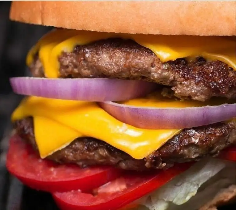 عکس نزدیک از یک همبرگر دوبل چیزبرگر آبدار و لذیذ، با پنیر ذوب شده، پیاز، گوجه و کاهو، آماده در فست فود دی.