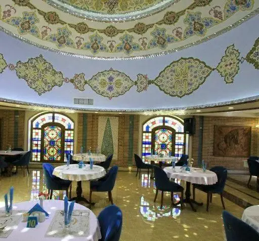 دکوراسیون داخلی رستوران ایرانی برمیس با سقف گنبدی و نقوش سنتی خیره‌کننده، پنجره‌های شیشه‌ای رنگی و فضایی دلنشین برای صرف غذا.