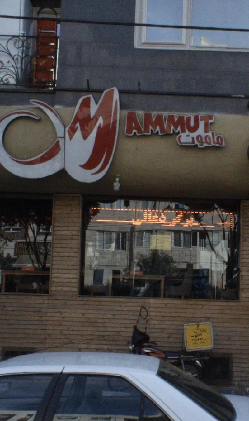 نمای بیرونی فست فود ماموت پلاس با تابلوی AMMUT و ماموت، پنجره ها، و موتور ارسال غذای رستوران برای خدمات تحویل.