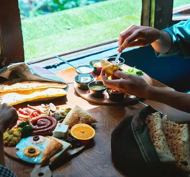 کافه آموره: یک میز صبحانه مفصل و لذیذ با نان تازه، تخم مرغ، پنیر، گوشت‌های سرد و دیپ‌های خوش طعم در محیطی آرام و با چشم‌انداز دل‌باز.