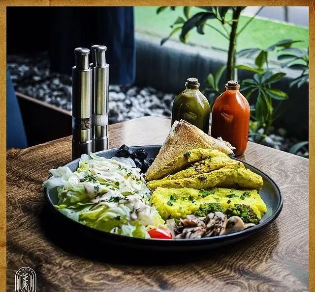 لذت صبحانه سالم و خوشمزه در کافه آموره: بشقاب کامل املت، سالاد تازه، قارچ، بروکلی، زیتون و نان تست بر روی میز چوبی.