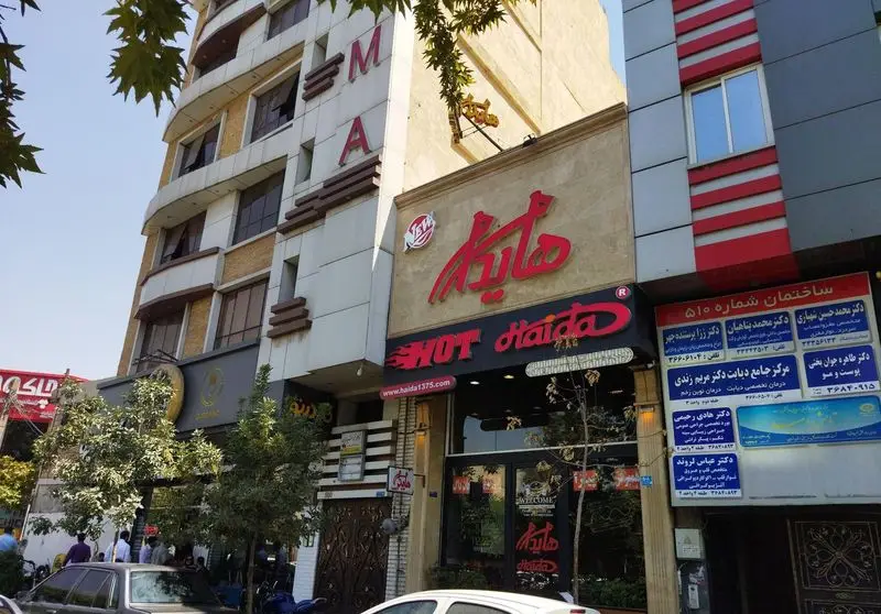 تصویری از نمای بیرونی فست فود هایدا در خیابان پیروزی تهران، با تابلوی بزرگ و قرمز رنگ هایدا و Hot Haida، در یک روز آفتابی.