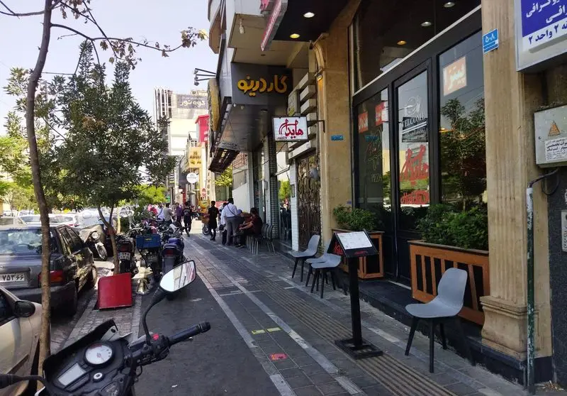 نمای بیرونی فست فود هایدا شعبه پیروزی در یک روز آفتابی، با مردم و ماشین‌های پارک شده در کنار خیابان شلوغ تهران.